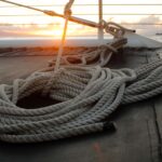 ein Seil liegt angeknotet auf einem Segelboot zusammengerollt , im HIntergrund ist ein Sonnenuntergang zu sehen.