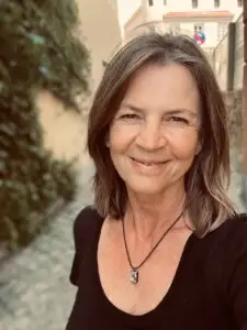 Karin Schaurhofer ist zu sehen im Freien, zwischen zwei Häusern in einer Gasse, sie ist schwarz gekleidet und strahlt positiv in die Kamera.